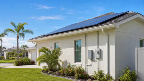 Florida stucco home with rooftop solar panels and utility meter equipment in bright sun